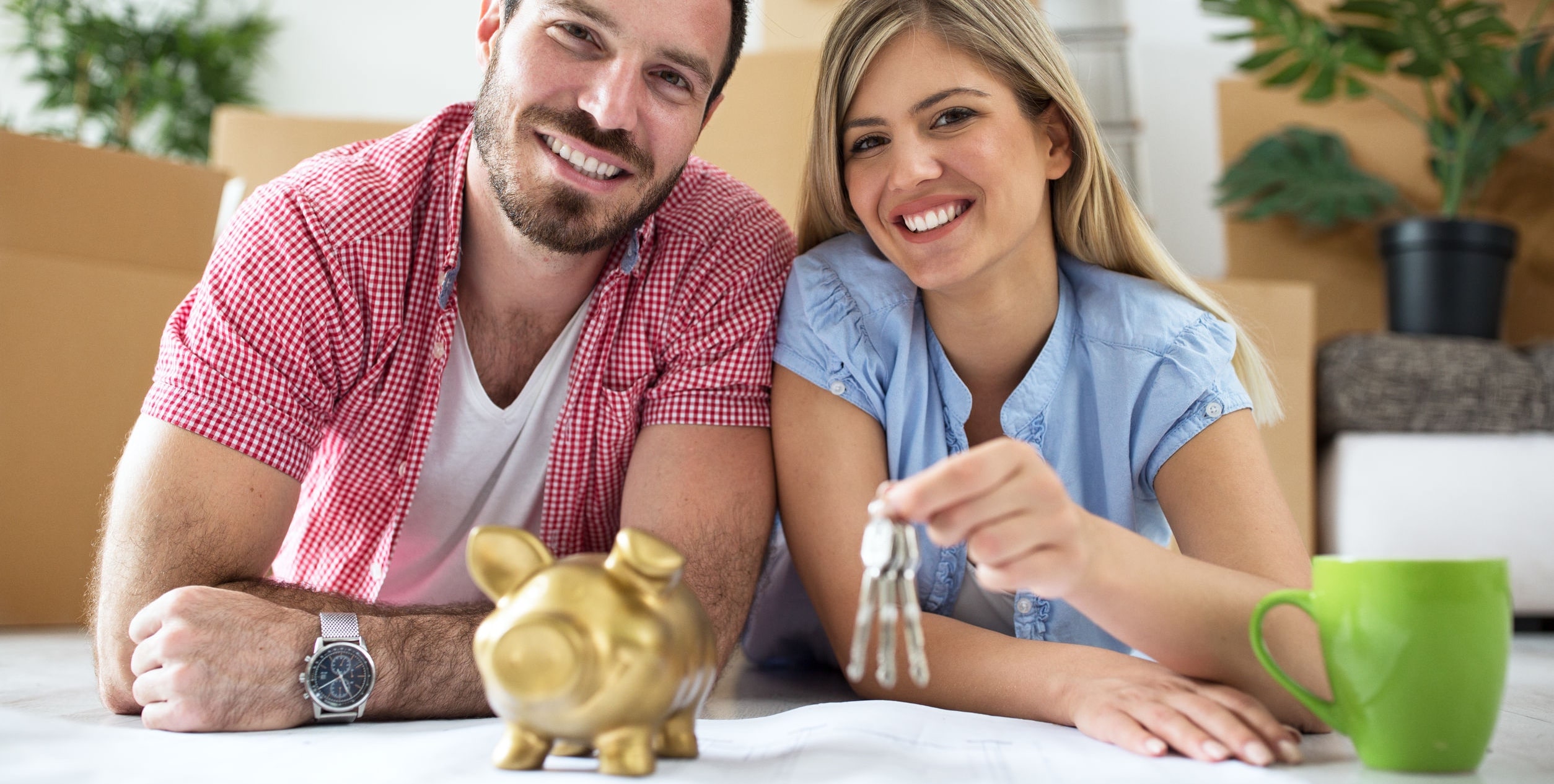 Couple holding keys to new house in front of piggy bank